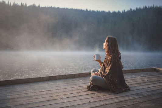 Femme au bord d'un lac qui boit une infusion