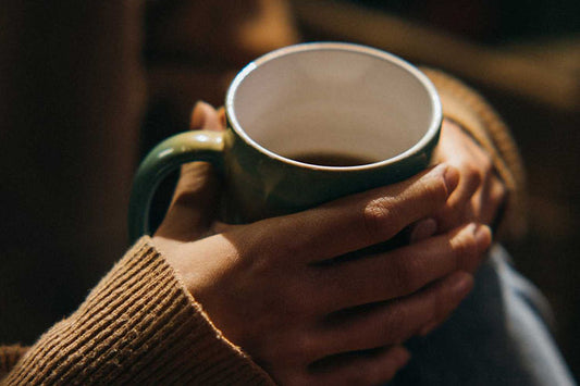 Femme qui tient à deux mains une tasse d'infusion