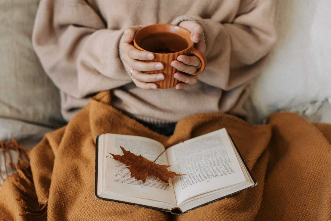 Femme qui tient une tasse avec un plaid et un livre ouvert