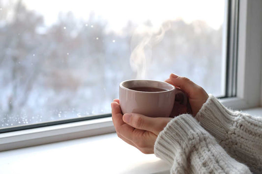 Femme tenant une tasse devant une fenêtre en hiver